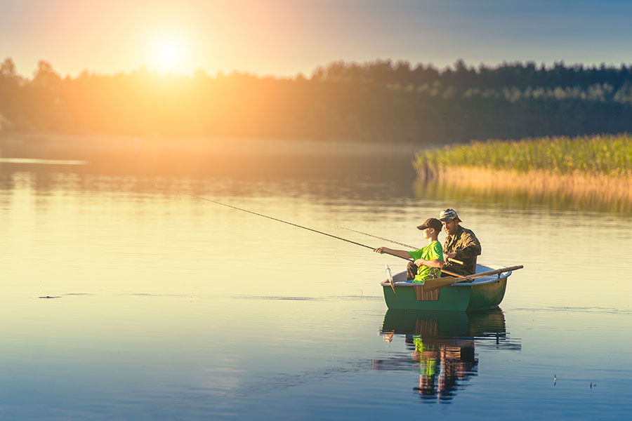 A father and son catch fish from a boat at sunset