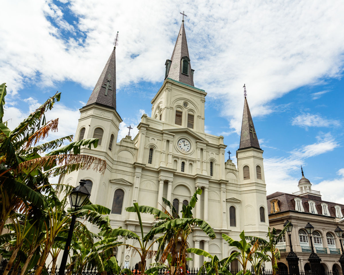 A white cathedral with three spires stands against a blue sky and clouds. 