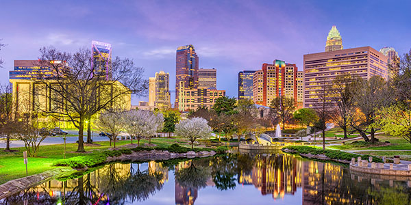 Purple skies over an urban landscape with a pond and trees in the city.