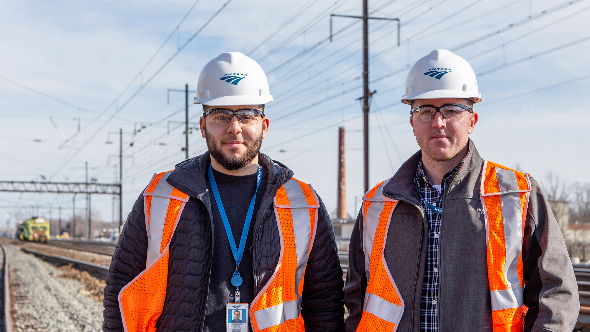 Two Amtrak employees in hard hats stand in the rail yard.
